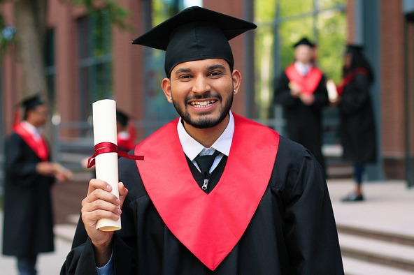 a person smiles in a graduation cap and gown while holding a diploma