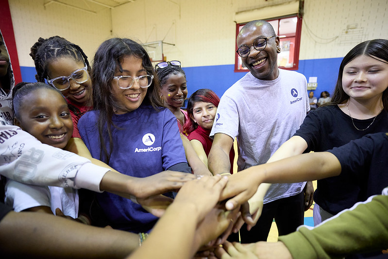 A diverse group of youth with two AmeriCorps members in a youth center gymnasium, a possible placement for LUK AmeriCorps YouthThrive Ambassador Program participants. 