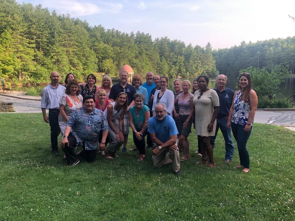 Leadership Team Members Join the Board of Directors for a group photo in a grassy area of a park in front of a lake