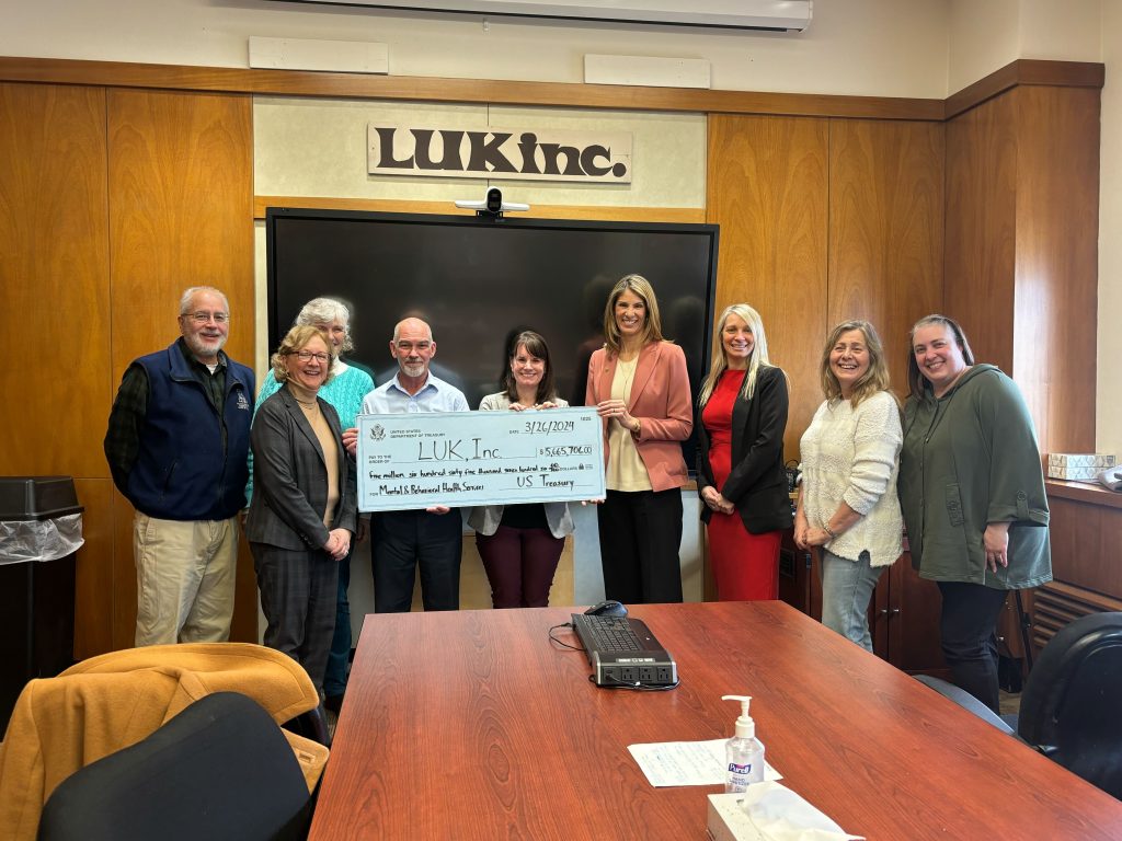Congresswoman Lori Trahan (MA-03), Fitchburg Mayor Sam Squailia, LUK CEO Beth Barto and members of LUK staff pose in a conference room with a large check addressed to LUK for 5,665,706 from the US Treasury for Mental & Behavioral Health Services
