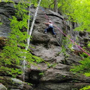 A woman climbing a natural crag with a top rope, with the staff on belay off screen